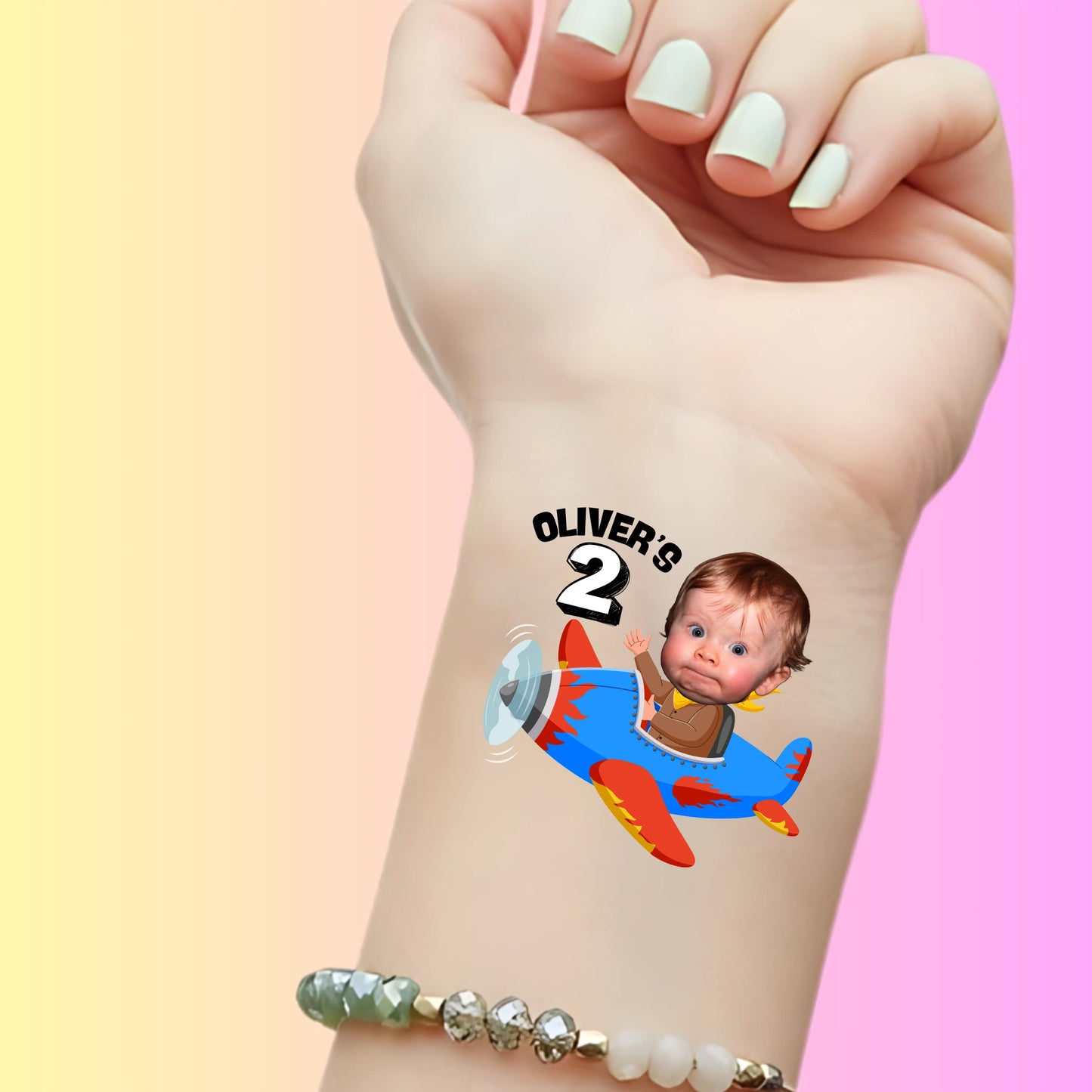 Custom temporary tattoo on wrist of toddler's face in cartoon airplane with text Oliver's 2 for birthday party favor